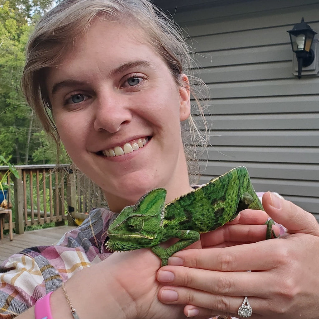 Person holding a green lizard outdoors with a house in the background